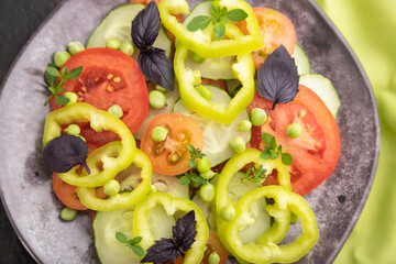 Vegetarian salad from green pea, tomatoes, pepper and basil on a green textile. Top view, selective focus.