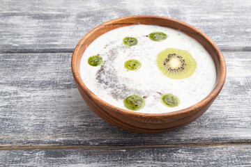 Yogurt with kiwi, gooseberry, chia and almonds in wooden bowl on gray wooden background. side view.