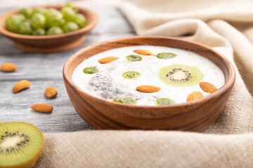 Yogurt with kiwi, gooseberry, chia and almonds in wooden bowl on gray wooden background. Side view, close up, selective focus.