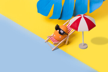 Minimal  funny composition with Easter egg with sunglasses sitting on deck chair and sun umbrela on...