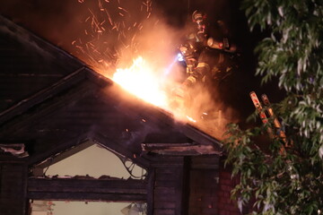 Structure fire ventilation and firefighting at night with flames.