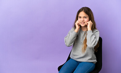 Little caucasian girl sitting on a chair isolated on purple background frustrated and covering ears