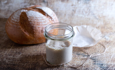 Sourdough in a glass jar and homemade bread on an old table.