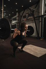 Obraz na płótnie Canvas Vertical shot of a sportswoman doing barbell squats at the gym