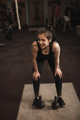 Fototapeta na wymiar Vertical shot of a sportswoman smiling joyfully, resting after working out with kettlebells