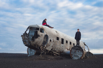 two guys standing on top of wreck of crashed abandoned airplane in a lava field black sand beach of...