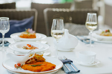 Lunch tablecloth with food and glasses of white wine with tea set in the restaurant. Focus is at the glass.
