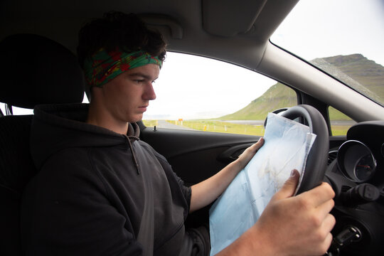 Teen guy planing a trip using a map while sitting behaind steearing wheel of car 