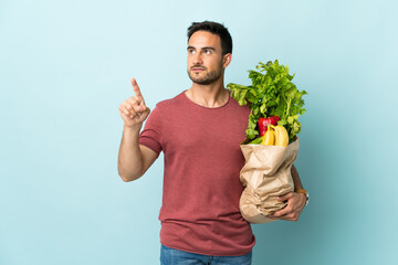 Young caucasian man buying some vegetables isolated on blue background touching on transparent screen