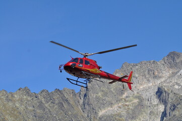Fototapeta na wymiar A red helicopter that flies in the mountains and transports wounded or material