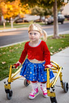 Disability photo of a cute little disabled girl walking with a special walker outdoors on the sidewalk