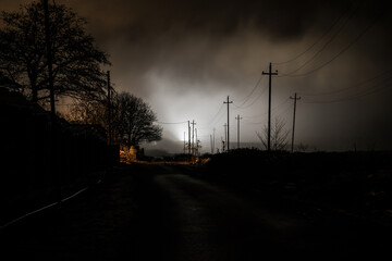 Night street country road with buildings and fences covered in fog lamp . Or Mysterious night in...