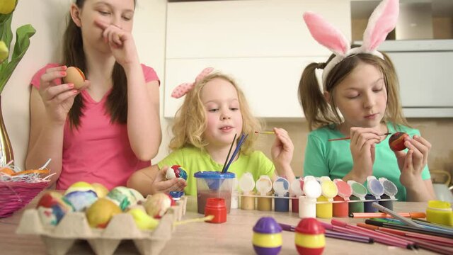 Happy beautiful cute girls sisters decorate the house in the kitchen Easter eggs with paint and markers. 4k video.