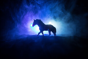 Beautiful horse running in desert at night. Silhouette of a horse miniature standing at foggy night. Creative table decoration with colorful backlight with fog. Selective focus