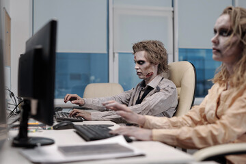 Zombie businessman sitting in front of monitor with dead female colleague working next to him