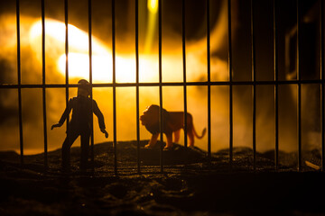 Silhouette of a lion miniature standing in a zoo cage dreams of freedom. Creative decoration with colorful backlight with fog.