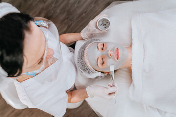 Esthetician or facialist applying a clay facial mask to woman