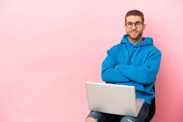 Young man sitting on a chair with laptop keeping the arms crossed in frontal position
