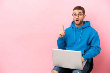 Young man sitting on a chair with laptop thinking an idea pointing the finger up