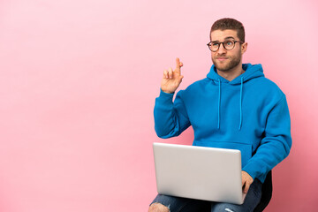 Young man sitting on a chair with laptop with fingers crossing and wishing the best