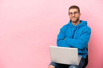 Young man sitting on a chair with laptop with arms crossed and looking forward