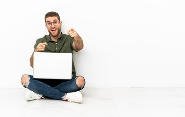 Young man sitting on the floor surprised and pointing front