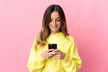 Young Romanian woman isolated on pink background sending a message or email with the mobile