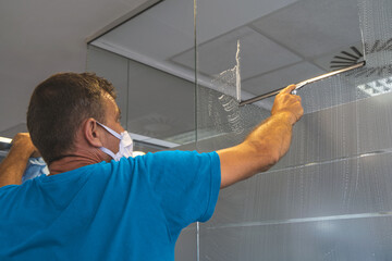 Professional cleaner with the face mask cleans the glass surfaces with the squeegee