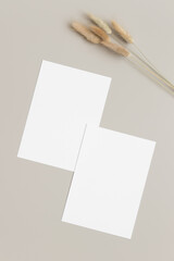 Two white invitation cards mockup with a lagurus decoration on the beige table. 5x7 ratio, similar...