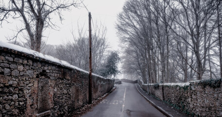 Fototapeta na wymiar Picturesque Snowy Lane with Ancient Irish Stonework Walls and bare forest