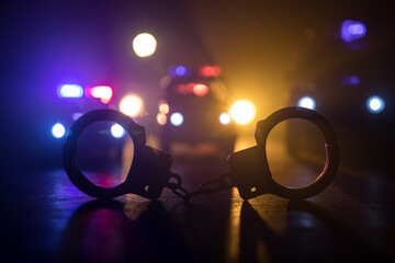 Police raid at night and you are under arrest concept. Silhouette of handcuffs with police car on...