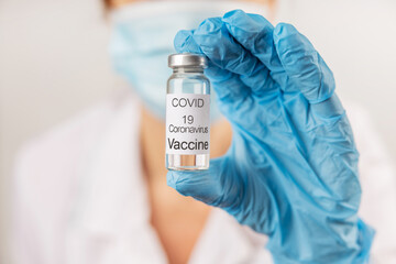 Vial with COVID-19 vaccine against coronavirus infection in the hand of a doctor in a nitrile glove on a white background. Close-up. Fight against coronavirus concept