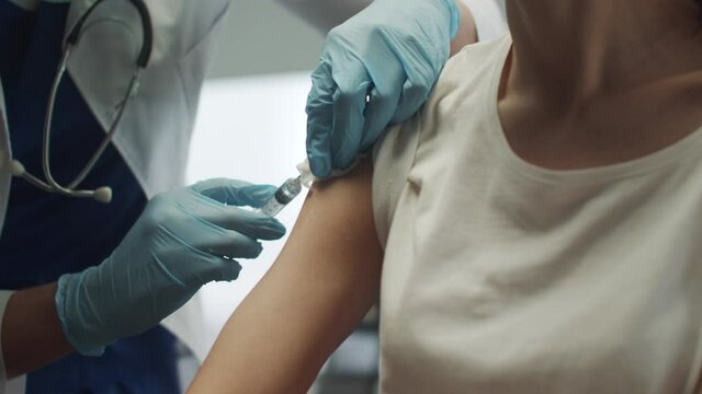 The patient receives a vaccination against the okved - 19 virus strain in her arm. The doctor lubricates the hand with alcohol to give the injection.
