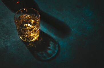 Contemporary still life with whiskey, scotch or bourbon glass with ice on textured blue background...