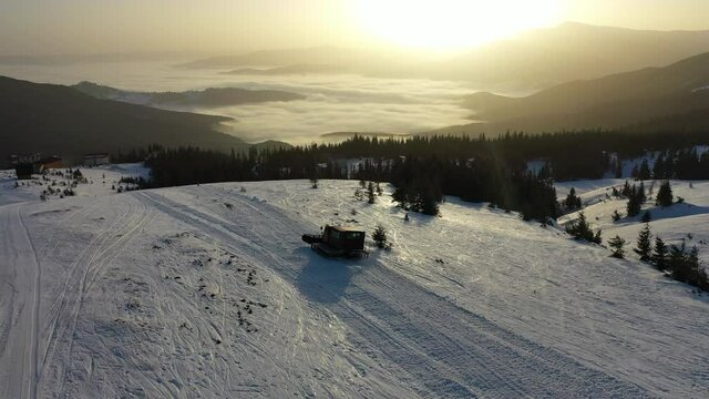 top view of a snowcat riding on white snow among mountain fir trees against the background of the rays of the dawn sun. freeride tours in a ski resort, transport