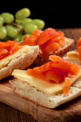 Smoked salmon sandwich with cheese and green grapes on a wooden board. Close up, Selective focus. Black background.