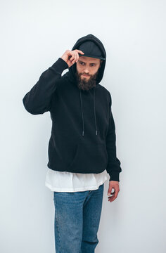 Portrait of handsome bearded hipster guy wearing black blank hoodie and baseball cap with space for your logo or design. Mockup for print. Hoodie design and advertising concept.