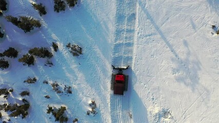 Aerial view of a snowcat cleans a ski slope, shovels snow into a bucket, winter mountain transport at a ski resort. Dawn rays of the sun - Powered by Adobe