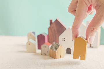Hand choosing yellow miniature house, searching right property in high demand housing boom, making decision on home investment concept © SewcreamStudio