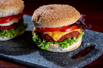 Tasty vegetarian food, homemade cheeseburgers made from plant based soya meat with cheese, onion, green lettuce and tomatoes