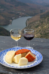 Taste of Portugal, variety of fortified port wines and goat and sheep cheeses, produced in Douro Valley with Douro river and colorful terraced vineyards on background in autumn, Portugal
