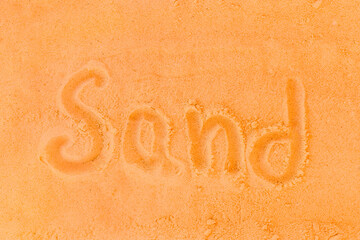 The word sand is written on a orange beach sand background. Sign or symbol of sand concept