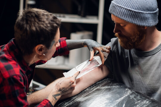 A tattoo artist bandages the young man's hand with a thin layer of petroleum jelly after applying the tattoo