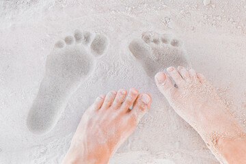 Traces of male and female legs on white beach sand background close-up