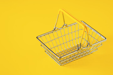 Empty metal wire shopping basket with yellow handles isolated on yellow background. Consumerism...