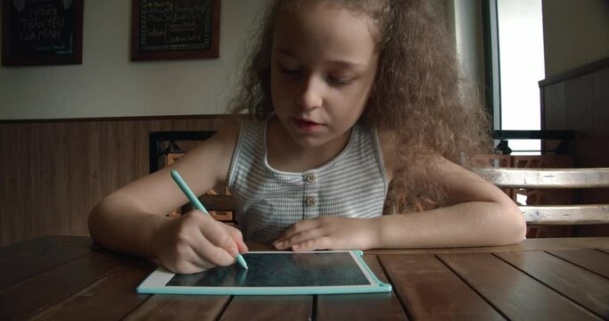 A portrait of a child sits at a table at home and draws on his tablet with a special pen, a preschooler uses a special tablet for drawing.