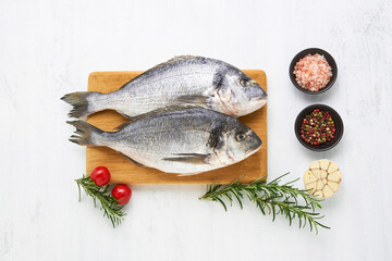 Raw dorado fish with spices on a wooden cutting board on a white background. Mediterranean seafood concept.