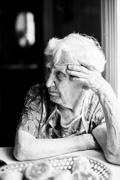 An old depressed woman sitting at the table. Black and white photo.