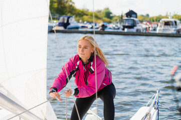 At the yacht parking lot, a young yachtsman in a pink windbreaker prepares her boat for a sailing...