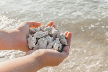 The girl's hands hold a pile of stones close up against the sea water